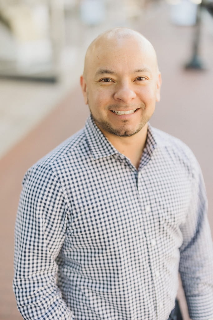 Pictured: Dr. Mateo Cruz; a bald, bearded man wearing a checkered shirt.