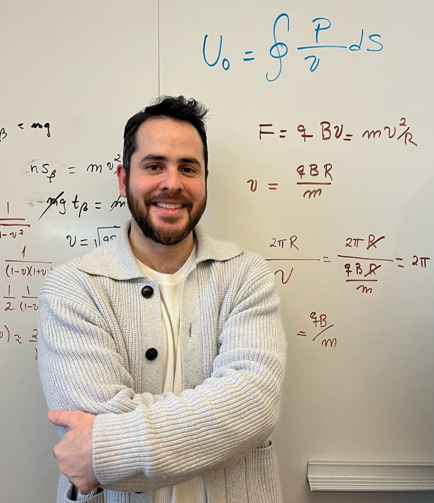 Vasquez stands in front of a white board with physics equations. 