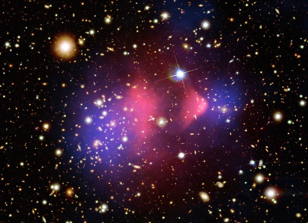 The Bullet Cluster. Splotches of blue and magenta against a black background.